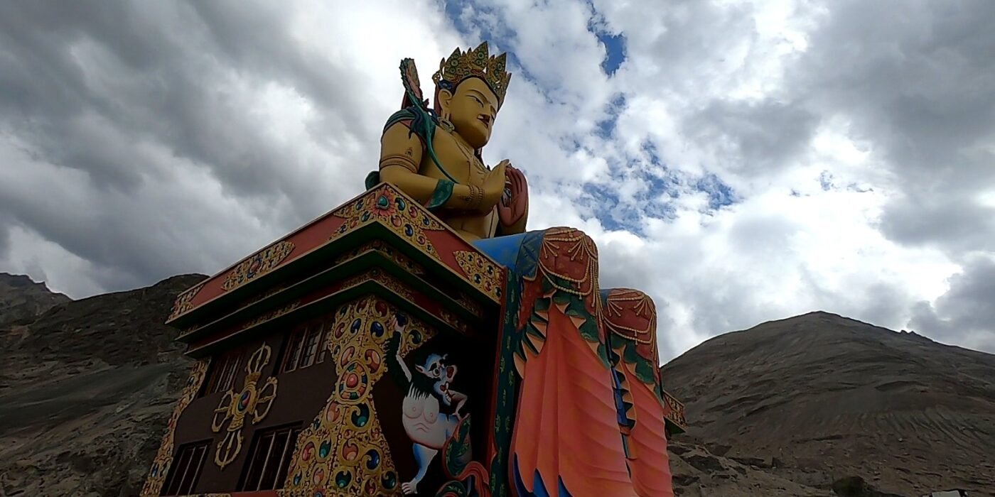 Giant colourful Buddha statue beside barren Himalayan mountains under a cloudy sky