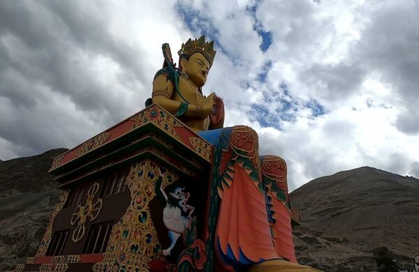 Giant colourful Buddha statue beside barren Himalayan mountains under a cloudy sky