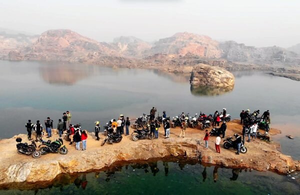 Group of riders and motorcycles gathered on a rocky ledge beside a lake during a group ride