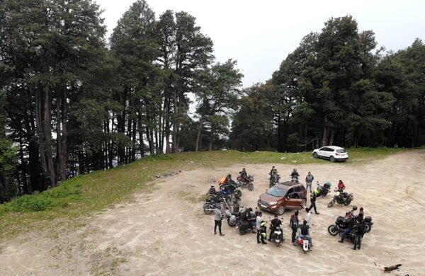 Riders and motorcycles gathered in a forest clearing among tall trees on a weekend getaway ride